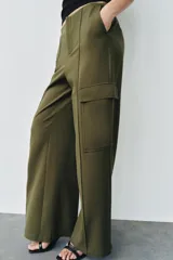 Pantalón cargo de tiro medio, color verde militar, con corte recto y bolsillos laterales de plastrón con solapa. Presenta detalles de nervios frontales y cierre con cremallera y gancho metálico.