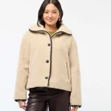 Campera de efecto borreguito en color beige, con cuello amplio y cierre frontal de botones negros. Presenta ribetes negros en contraste en el cuello, la apertura frontal y los puños. Marca Kiabi.