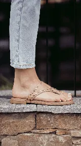 Sandalias chatas de cuero color bordó, con diseño de tira ancha que envuelve el empeine y sujeta el dedo gordo, decoradas con tachas metálicas doradas.