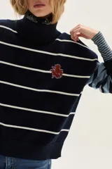Sweater de cuello tortuga, tejido a rayas horizontales azul marino y blanco. Presenta un bordado de flor roja en el pecho y mangas largas con diseño de rayas en tonos de azul más claro.