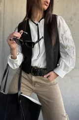Chaleco negro de gamuza sintética, de estilo boho-chic, con costuras decorativas en los bordes y diseño clásico atemporal.