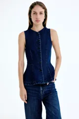 Chaleco de denim azul oscuro, sin mangas, con escote redondo y cierre frontal de botones oscuros. Presenta costuras moldeadoras y un diseño con peplum en la parte inferior.