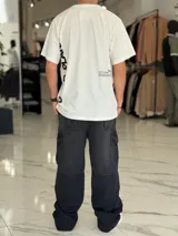 Remera oversize color beige, con mangas cortas y cuello redondo. Presenta un diseño estampado con texto en la parte trasera y lateral, de corte holgado y estilo urbano.
