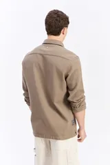Camisa de manga larga color beige, de tejido texturado con cierre frontal de botones y cuello camisero clásico.