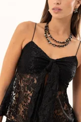 Top de encaje negro con breteles finos, escote con detalle de nudo frontal y diseño con apertura central.