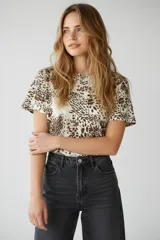 Remera de manga corta con cuello a la base y diseño holgado, confeccionada en algodón con elastano y estampado animal print en tonos marrones sobre fondo claro.