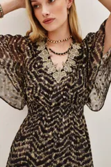 Vestido midi de tejido fluido con estampado en zigzag en tonos oscuros y dorados. Presenta un escote en V decorado con encaje, mangas cortas tipo mariposa, cintura elástica y una abertura frontal en la falda.