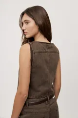 Chaleco corto de denim negro con escote en V y diseño sin mangas. Presenta terminación lavada y detalles laterales con entramado y tachas metálicas que aportan un toque distintivo.
