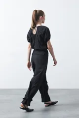 Pantalón baggy negro de silueta relajada con volumen amplio y caída fluida. Presenta detalles de ajuste con hebillas metálicas en el bajo y un cinturón de tela con hebilla metálica en la cintura.