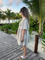 Vestido corto color beige de lino, con cuello mao, mangas cortas con volados, tablas en el canesú y falda escalonada con volantes.