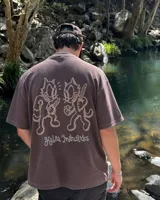 Remera marrón oversize de manga corta con estampado gráfico en la espalda de dos gatos de estilo retro con cuchillos y texto "Kahoa Industries".