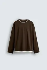 Camiseta de manga larga y corte relajado en color marrón oscuro. Presenta un diseño de doble capa en el cuello y el ruedo, con un borde interior en color blanco que crea un efecto de contraste.
