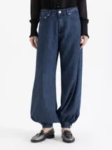 Jeans de mezclilla azul oscuro, modelo balloon con tiro alto, pierna muy ancha y puños ajustables con botón en el tobillo para crear volumen.