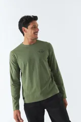 Remera verde militar de manga larga, cuello redondo y corte recto. Estampa pequeña en el pecho con texto en negro.
