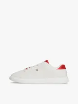 Zapatillas Tommy Hilfiger de diseño clásico y bajo, color blanco con detalles en rojo en la parte trasera del talón y en la lengüeta. Presentan cierre de cordones y el logo metálico distintivo de la marca en el lateral.