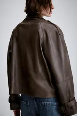 Cazadora de Zara Woman Collection confeccionada en material efecto piel color marrón oscuro. Presenta cuello con solapas, cierre frontal cruzado con botones, bolsillos delanteros y mangas largas con trabillas y hebillas ajustables en los puños.