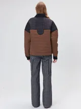 Campera acolchada con diseño de bloques de color en tonos terracota y beige. Presenta cuello camisero y puños en pana negra, cierre frontal oculto con botones a presión y costuras capitoneadas en toda la prenda.