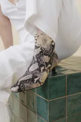 Botín blanco con estampado de piel de serpiente, punta fina y taco chupete. Cierre con cremallera en la parte trasera.