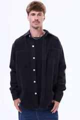 Camisa de hombre de manga larga en color negro, confeccionada en denim con efecto lavado. Presenta cuello clásico, cierre frontal con botones a tono y dos bolsillos frontales con solapa en el pecho.