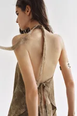 Top de cuello halter con tiras cruzadas para atar al cuello, hombros descubiertos y bajo asimétrico con caída drapeada y textura rústica con estampado sutil.