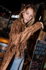 Chaqueta de gamuza marrón con diseño de flecos en la parte delantera y las mangas, corte tipo camisa y cierre frontal de botones.