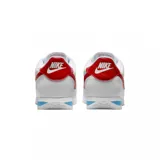 Championes Nike modelo Cortez, de diseño clásico en color blanco con el icónico swoosh lateral en rojo. Presenta detalles en rojo en el talón y una franja azul en la entresuela, con suela dentada característica.