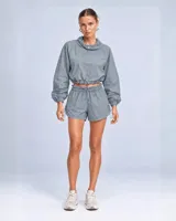 Conjunto deportivo de dos piezas color durazno, compuesto por un buzo cropped de manga larga con cuello alto ajustable y cintura regulable, y un short con cintura clochard y cordones laterales.