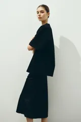 Pollera midi negra de tiro alto con elástico oculto en la cintura y leve vuelo en el bajo. Presenta un leve brillo y caída suave, sin forro.
