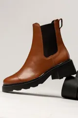 Bota tipo Chelsea de cuero color verde oliva, con paneles laterales elásticos negros y suela track de goma negra con taco cuadrado.