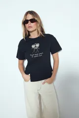 Remera blanca de manga corta con estampa frontal de un personaje con lentes de sol y la frase "Llegué tarde porque no quería venir". Tiene silueta relajada y calce cómodo, con un corte asimétrico en el bajo.