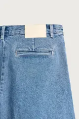 Bermuda de denim con corte relaxed fit, tiro medio y pierna recta. Presenta pliegues frontales dobles, bolsillos laterales y bolsillos traseros de doble vivo. Confeccionada en tejido rígido con efecto lavado, cierre frontal con cremallera y botón.