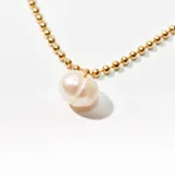 Collar dorado con cadena de bolitas y dije de perla irregular.