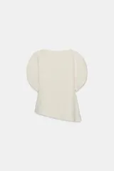 Top color crema de cuello redondo y manga corta abullonada. Presenta un bajo asimétrico y cierre en la espalda con cremallera oculta en la costura.