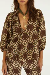 Blusa de corte relajado color marrón con estampado floral de margaritas, escote en V con cordones colgantes y mangas tres cuartos abullonadas con puños elastizados.