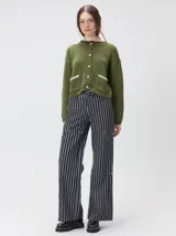 Cardigan de algodón grueso en color rojo, con cuello redondo y cierre frontal de botones grandes. Presenta bolsillos cuadrados en el bajo con detalles de pelo sintético en los bordes y logo bordado en uno de ellos. Posee puños y ruedo elastizados con diseño holgado.