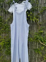 Mono largo de corte holgado con diseño de rayas verticales finas en azul y blanco. Presenta breteles anchos para atar sobre los hombros y piernas de corte ancho tipo palazzo.