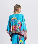 Kimono abierto de manga corta amplia, confeccionado en viscosa con estampado tropical de tucanes y palmeras sobre fondo celeste, con detalles en rosa, amarillo y negro, y terminación de flecos en los bordes.