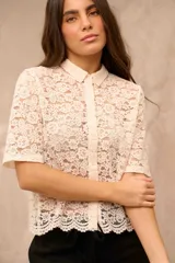 Camisa de encaje color crema, con cuello camisero, mangas cortas y cierre frontal con botones.