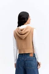 Chaleco de punto color beige, de corte corto y holgado. Presenta capucha, cierre frontal completo y terminaciones acanaladas en la cintura.