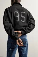 Cazadora cropped fit de color negro para hombre, con cuello solapa y detalles combinados en tejido efecto piel. Presenta mangas largas, bolsillos de doble vivo en la cadera, cierre frontal con botones a presión y puños y cintura elásticos ribeteados.