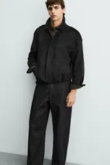 Cazadora cropped fit color verde militar, confeccionada en tejido efecto ante. Cuenta con cuello solapa, manga larga con puño abotonado, trabillas en los hombros, bolsillos laterales ocultos y un bolsillo interior. El bajo tiene elástico interior y el cierre frontal es con cremallera oculta por solapa con botones a presión.