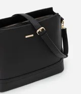 Cartera tipo hobo de tamaño pequeño, confeccionada en material sintético color marrón oscuro con acabado liso. Presenta una correa ajustable, cierre principal con cremallera y detalles metálicos dorados, incluyendo una placa con el logo de la marca en el frente.