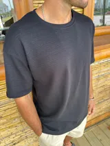Remera de corte oversize color negro, confeccionada en tejido de punto con textura de líneas horizontales en relieve. Presenta cuello redondo y mangas cortas.