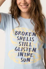 Remera de manga corta color beige, confeccionada en 100% algodón, con cuello redondo y estampa frontal con texto en tonos rosados.