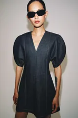 Vestido corto de denim con escote en pico, mangas cortas abullonadas con aberturas y costuras con pespuntes a contraste. Cierre posterior con cremallera.