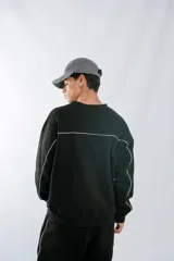 Buzo negro de corte holgado con cuello redondo, confeccionado en frisa invisible premium. Presenta detalles de vivos en color blanco en los laterales y en la espalda, y cuenta con una etiqueta decorativa en el frente.