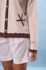 Cárdigan de tejido punto color crema con cuello y ribetes en marrón oscuro. Presenta botones frontales y bordados de estrellas de mar en el frente.