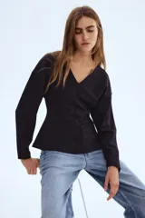Top negro de tejido suave con efecto neopreno, escote en V, hombros caídos y mangas largas con puños ceñidos. Presenta una cintura entallada que realza la figura.