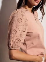 Remera de algodón color rosado con mangas cortas abullonadas de broderie con diseño floral calado. Presenta cuello redondo y costura vertical central en el frente.