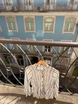 Camisa de manga larga con diseño a rayas verticales en tonos azul, gris y crema. Presenta un cuerpo con frunces elásticos decorativos, cuello con volados y puños con elástico y terminación en volado. Incluye cierre frontal con botones.